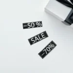 Kotak hadiah elegan dengan pita hitam di atas marmer bersama stiker diskon, menggambarkan promo buy 2 get 1